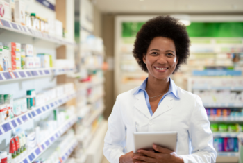 Smiling pharmacist standing in front of stocked shelves 